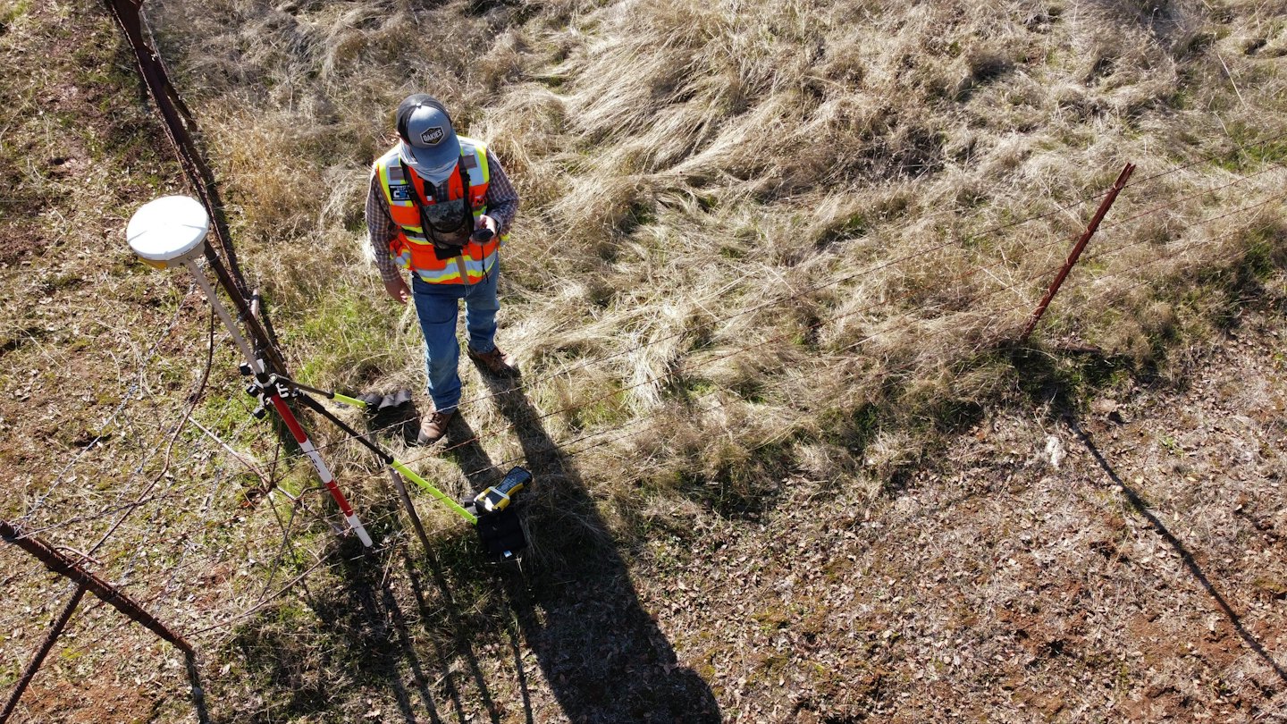 Geodet pracuje s vybavením na slnečnom, trávnatom poli.